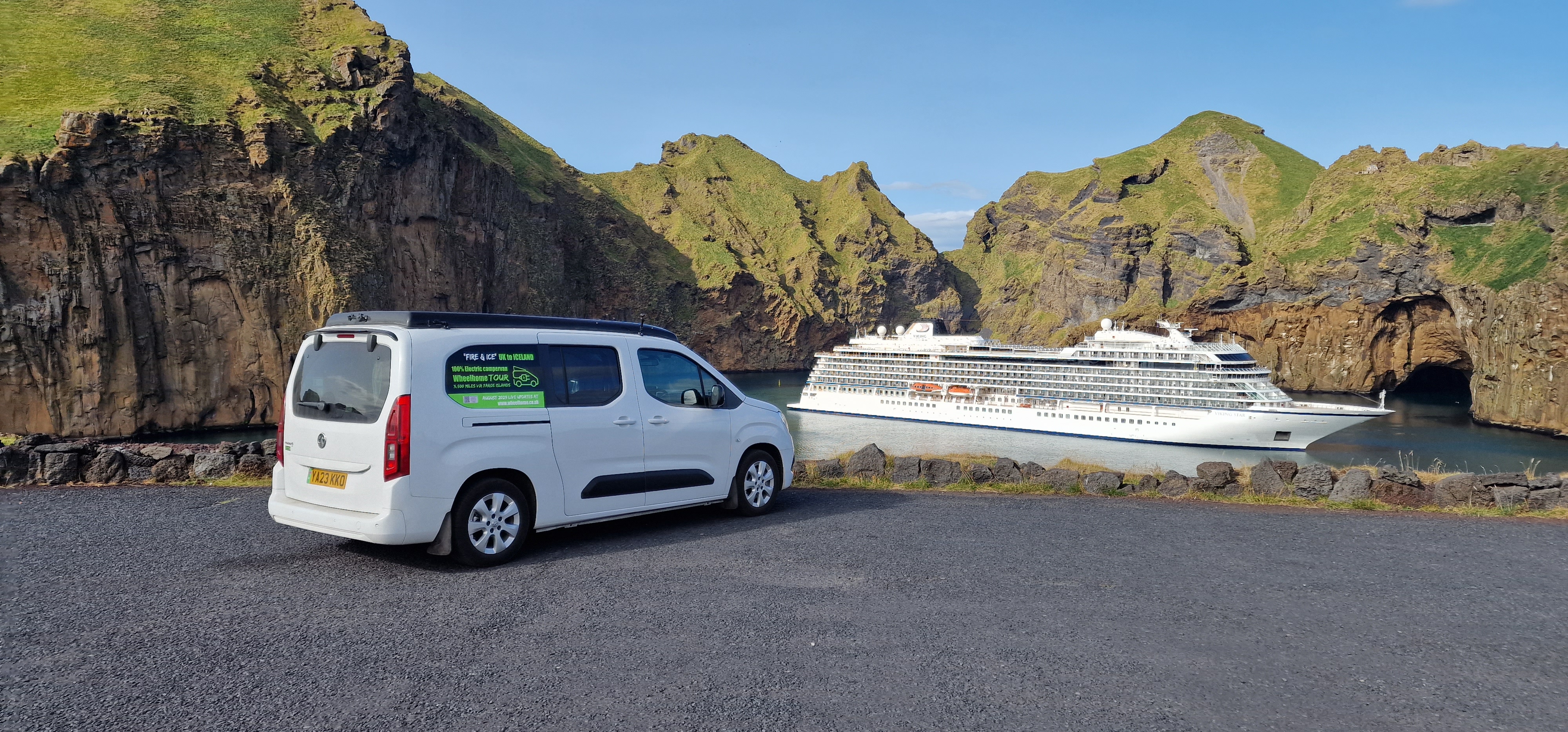 Electric campervan at Heimaey harbour with cruise ship behind dramatic cliffs